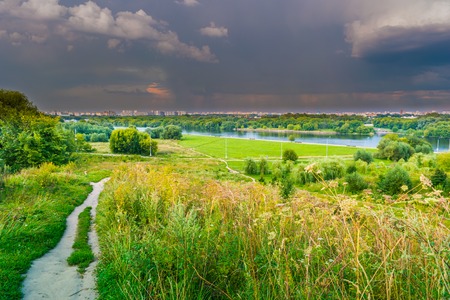 Pathway on a hill with wildflowers. Beautiful natural landscape at sunset with green grass, flowers and cloudy sky. Image of travelling and adventure in countryside. Great outdoors picture.の写真素材