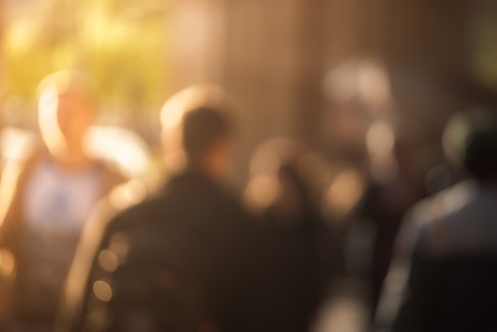 People walking down the street in the evening, beautiful light at sunset. The photo is purposely made out of focus, no faces are recognisibleの写真素材