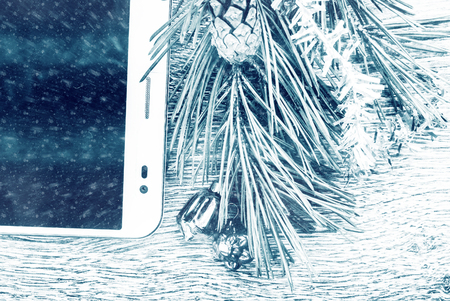 Tablet pc with blank screen and christmas fir tree with cones and christmas tree decoration on a wooden background. Template for banner or bavkground, or image for a blog.の写真素材