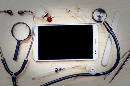 Tablet pc with medical objects on a desk as a metaphor for electronic diagnostic or healthcare mobile apps. Medical backgroundの写真素材