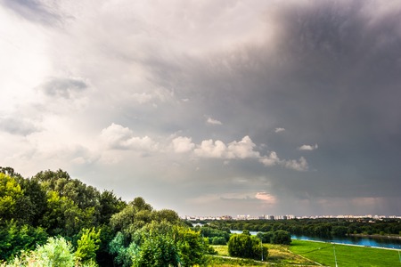 Beautiful natural landscape at sunset with green grass, flowers and cloudy sky. City building in distance. Image of recreation in countryside. Great outdoors picture.の写真素材
