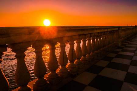 Leghorn (Livorno), Tuscany, Italy: promenade Mascagni Terrace at night, an elegant square on the coast with black and white checkered floor, columned bannister viewed against setting sunの写真素材
