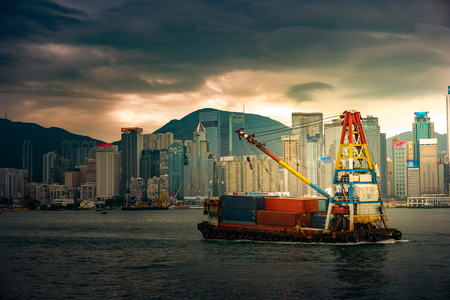 Hong Kong skyline with container vessel and a small tug boat in the forefront. Mooring operations in Hong Kongの写真素材