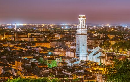 The white bell tower of the Cathedral of Verona in Italy at sunset. Night lights and purple sky above the famous italian city.の写真素材