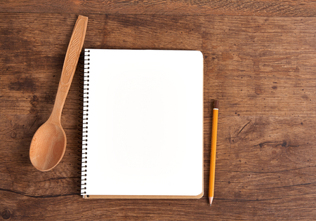 Open cookbook, wooden kitchen spoon and pencil on wood table backgroundの写真素材