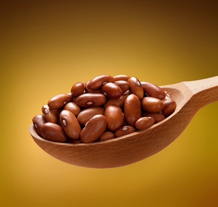Brown beans in a wooden spoon - beans on wooden spoon isolated on golden backgroundの写真素材