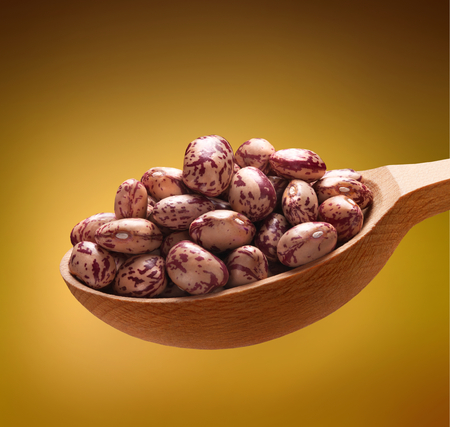 Speckled beans in a wooden spoon - beans on wooden spoon isolated on golden backgroundの写真素材