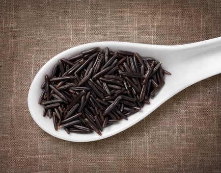 Black rice in white porcelain spoon / high-res photo of grain in white porcelain spoon on burlap...