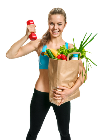 Happy cutie athletic woman showing biceps with grocery bag full of healthy fruits and vegetables  photo set of cheerful brunette girl with healthy dietary eco organic food over white backgroundの写真素材