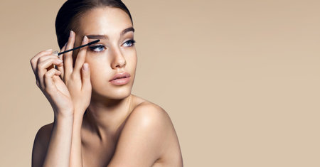 Mascara applying. Makeup closeup. Eyes make-up  photos of appealing brunette girl on beige...