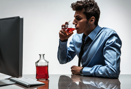 Young drunk caucasian businessman with bottle of alcohol  photo of businessman addicted to alcohol at the workplace, depression and crisis conceptの写真素材