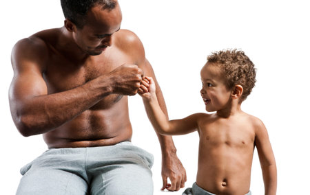 Fist bump, power five, dap, fist pound, or brofist. Together partnership greeting concept photos of sporty muscular Hispanic shirtless fitness man with his son over white backgroundの写真素材
