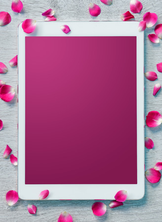 Digital tablet, pink screen with small petals on white wooden backgroundの写真素材