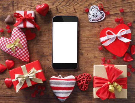 Smartphone with gifts and hearts on wooden table. View from above.の写真素材