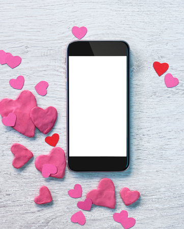 Smartphone with heap of small hearts on white wooden background.の写真素材
