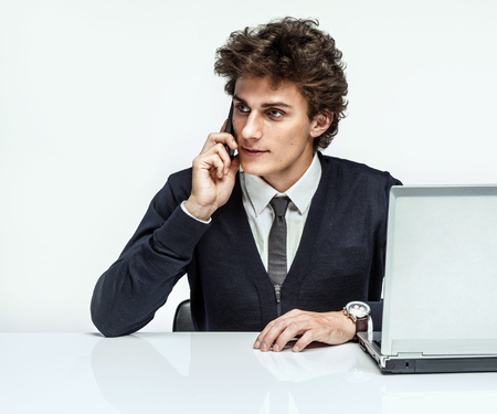 Businessman talking by cell phone while working with PC computer young man talking on the phone sitting in a desk on gray backgroundの写真素材