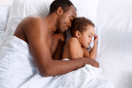Father and son sleeping in bed, family relationship. Hispanic man with his son in bedの写真素材