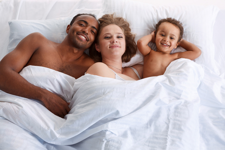 Happy family on white bed in the bedroom. Concept of cheerful American familyの写真素材