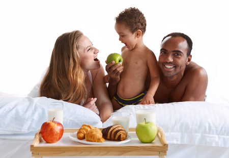 Charming family having breakfast in parents bed at home. Concept of cheerful American familyの写真素材