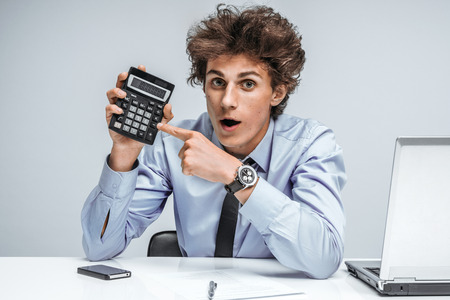 Geeky surprised businessman showing calculator / modern businessman at the workplace working, depression and crisis conceptの写真素材