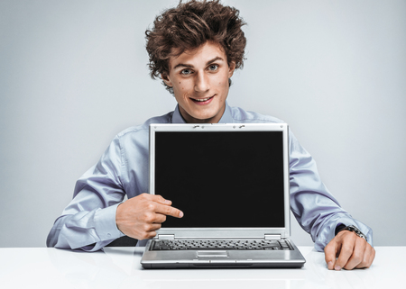 Smiling businessman at the workplace looking at camera and showing at screen laptop. Business conceptの写真素材