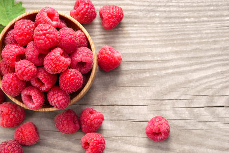 Sweet raspberries in bowl on wooden table. Close up, top view, high resolution product