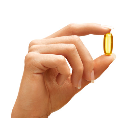 Woman's hand holding Omega 3 capsule isolated on white background. Close up. High resolution product.の写真素材