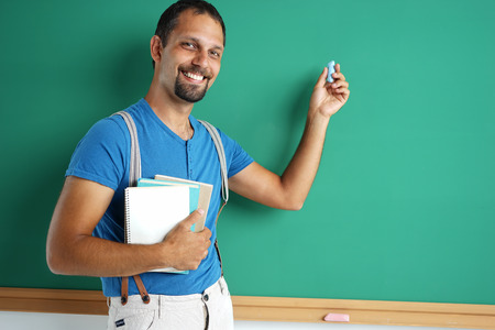 Exemplary student standing near blackboard with books and chalk. Photos adult student,  education conceptの写真素材