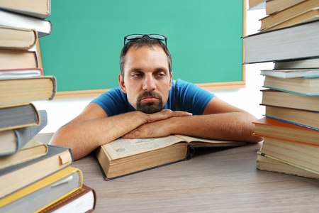 Boredom. Teacher resting his chin on his hands, laying on a table with opened book. Education conceptの写真素材