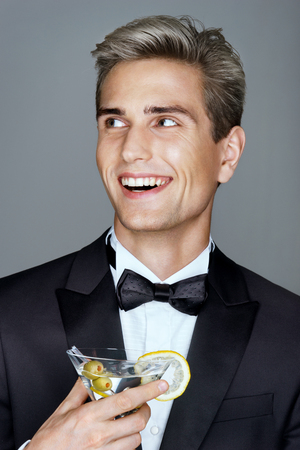 Laughing imposing man with glass of martini looking away. Photo of Stylish man in elegant black suit. High lifeの写真素材