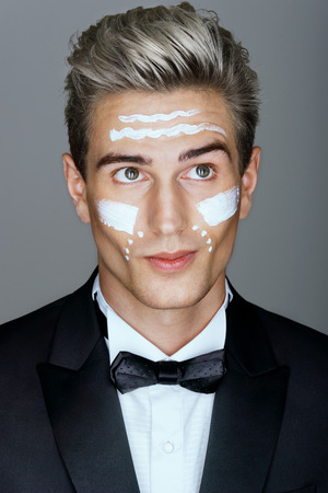 Beautiful face of imposing man with cosmetic cream on cheeks, spa treatment. Photo of man in black suit on gray background. Skin care concept.の写真素材