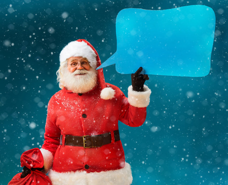 Santa Claus with sack of gifts showing sign speech bubble banner, looking happy excited. Happy Santa Claus on blue background. Merry Christmas & New Year's Eve concept.の写真素材