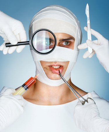 Patient in bandages and many hands holding medical instruments. Nurses holding magnifying glass, scalpel, syringe, surgical clamp near his face. Plastic Surgery conceptの写真素材