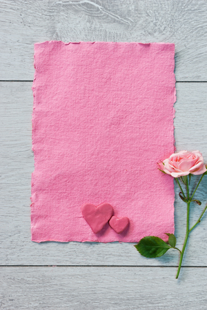 Pink card with pink heart shaped and rose on white wooden background. Top view. Valentines Day conceptの写真素材