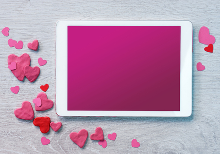 Digital tablet with heap of small hearts on wooden background. Copy space for your text. Top view. Valentines Day conceptの写真素材