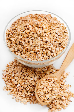 Uncooked oatmeal in glass bowl and spoon on white background. Healthy food. Close up, high resolution product.の写真素材
