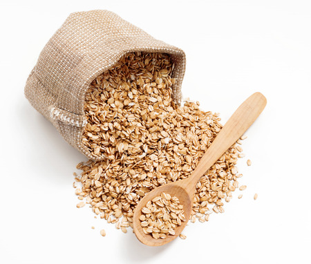 Uncooked oatmeal in wooden spoon and sack on white background. Close up, high resolution productの写真素材