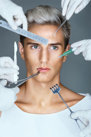 Many hands holding medical tools near face patient. Portrait of young man with surgical instruments. Concept of plastic surgeryの写真素材