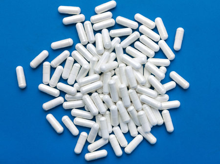 Heap of white capsules on blue background. Top view, high resolution product. Health care concept