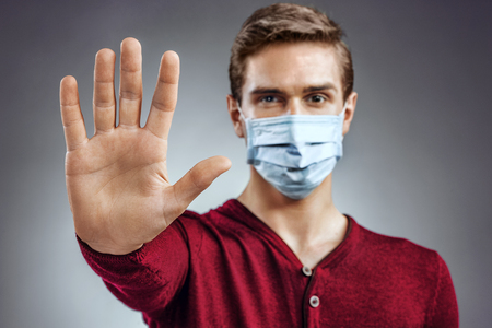 Stop the infection! Healthy man showing gesture "stop". Photo of man wear protective mask against infectious diseases and flu. Health care concept.の写真素材