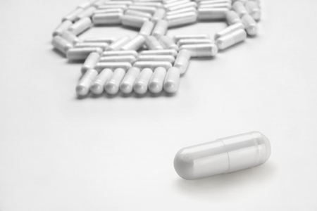 One white capsule and skull symbol, isolated on white background. Close up, high resolution product. Drug abuse conceptの写真素材