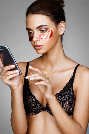 Pretty girl with red eye patches, looks on the phone. Photo of woman receiving spa treatments. Grooming himselfの写真素材