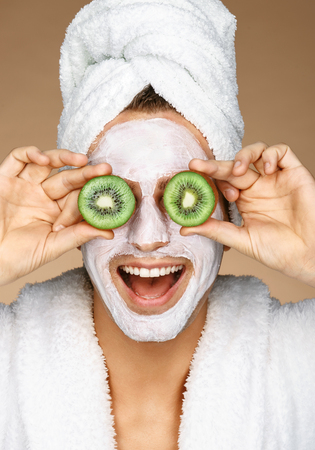 Funny young man with facial mask and pieces of kiwis on eyes. Photo of well groomed man receiving spa treatments. Beauty & Skin care conceptの写真素材