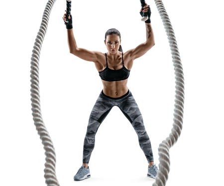Athletic woman working with heavy ropes. Photo of attractive brunette in sportswear isolated on white background. Strength and motivation.の写真素材