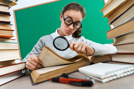 Student with a magnifying glass seeks the answer in book. Photo of girl keen on reading book. Education conceptの写真素材