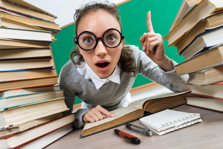 Student having good idea, pointing finger up. Photo of astonished young girl wearing glasses around books. Education conceptの写真素材
