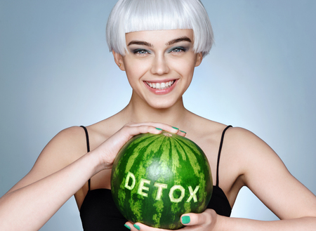 Happy girl with green watermelon. Photo of smiling blonde girl on blue background. Detox conceptの写真素材