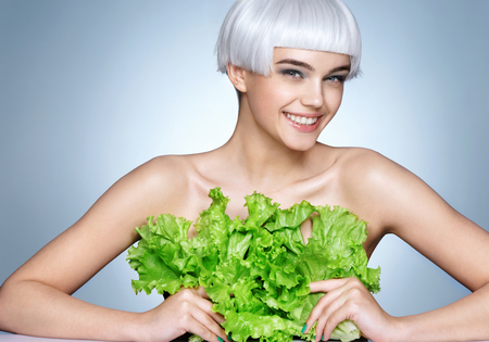 Pretty girl covering her breast a lettuce leaves. Photo of fashion blonde girl on blue background. Detox conceptの写真素材