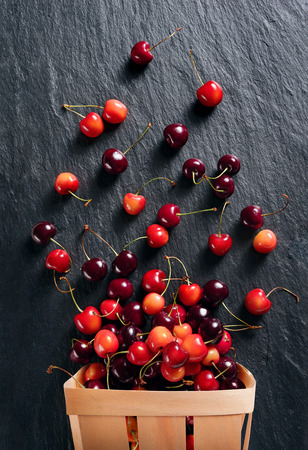 Cherry explosion. Photo of cherry in basket on black slate. Top view. High resolution product.の写真素材
