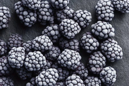 Frozen blackberry on black slate. Close up. Top view. High resolution product.